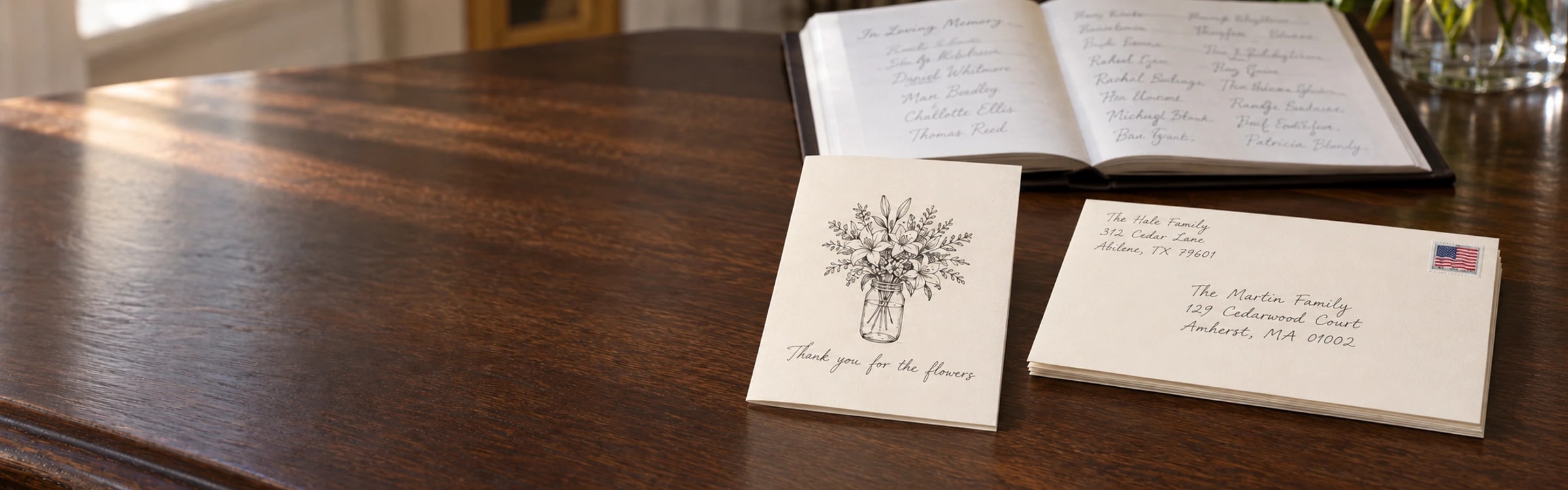 A hand-drawn funeral thank-you card open in front of a stack of addressed envelopes and a register book